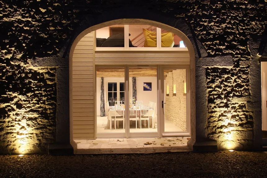 Façade en pierre du Clos et baie vitrée éclairées à la tombée de la nuit